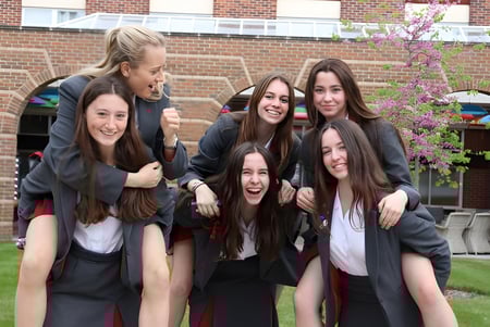 Un grupo de alumnas de la Battle Abbey School en togas se encuentra frente a un edificio de ladrillo con un árbol en flor.
