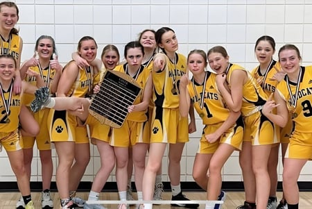Un grupo de jóvenes jugadoras de baloncesto en camisetas amarillas posan en la Bawlf School frente a una pared de azulejos.