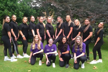 Un grupo de jóvenes mujeres con atuendos negros está de pie en el campus del Baxter College en medio de la vegetación.