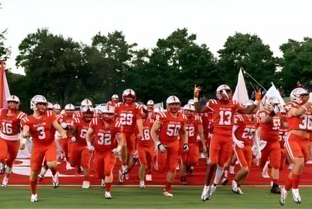 Un grupo de jugadores de fútbol en camisetas rojas corre por el campo en las instalaciones de la Baylor School.