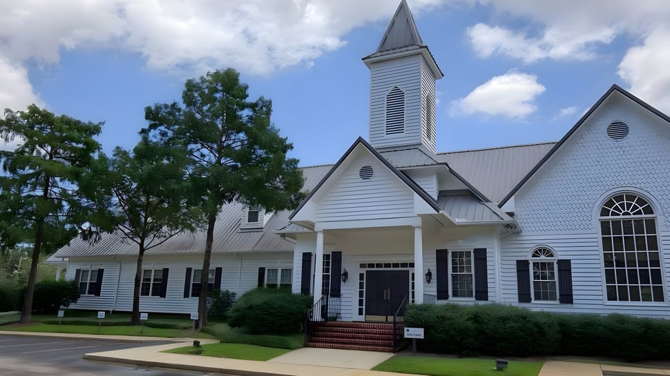 Una iglesia de madera blanca con un alto torre se encuentra en el terreno de la Bayshore Christian School en una área cubierta de hierba.