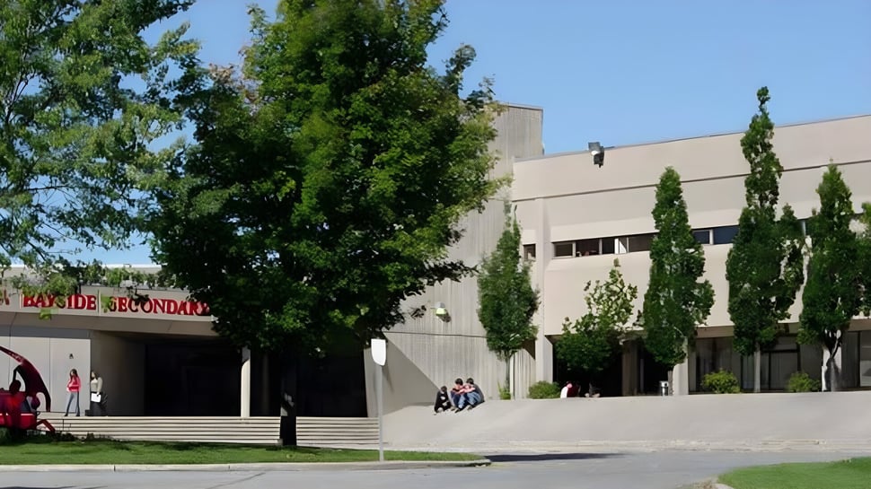 El moderno edificio de varios pisos de la Bayside Secondary School está rodeado de árboles y áreas verdes.