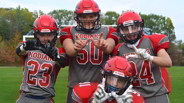 Cuatro jugadores de fútbol están en el campo de la Bear Creek Secondary School frente a árboles en el fondo.