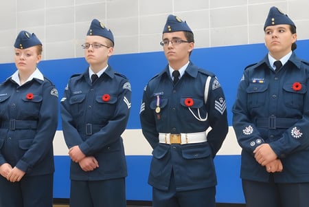 Cuatro estudiantes de la École Secondaire Beaumont Composite High School están en uniformes militares frente a un fondo azul.