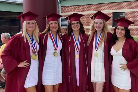 Cinco graduadas en togas rojas de la Beaver Area High School posan con diplomas frente a un edificio de ladrillo.