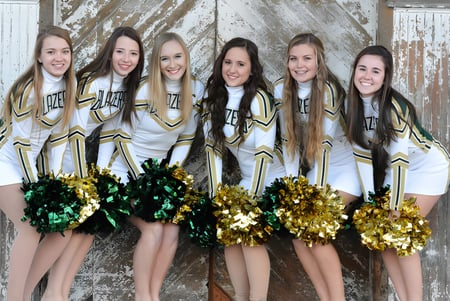 Un grupo de animadoras de la Beckman Catholic School posan con pompones dorados y verdes frente a un fondo de madera desgastada.