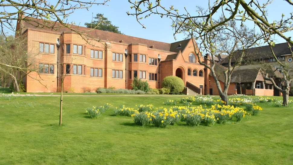 El edificio de ladrillo de varios pisos de la Bedales School está rodeado de una pradera con narcisos amarillos.