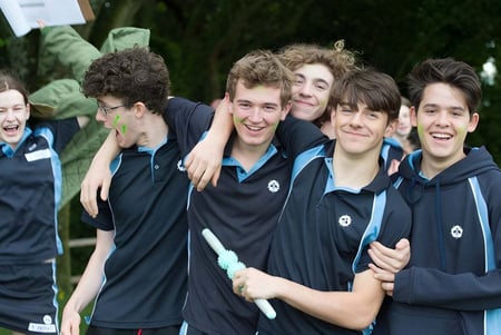 Un grupo de estudiantes de la Bedales School lleva uniforme escolar y está frente a un fondo verde.