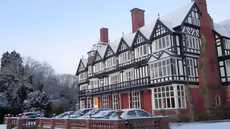 El histórico edificio Tudor de Bedstone College está rodeado de árboles cubiertos de nieve y un cielo azul claro.