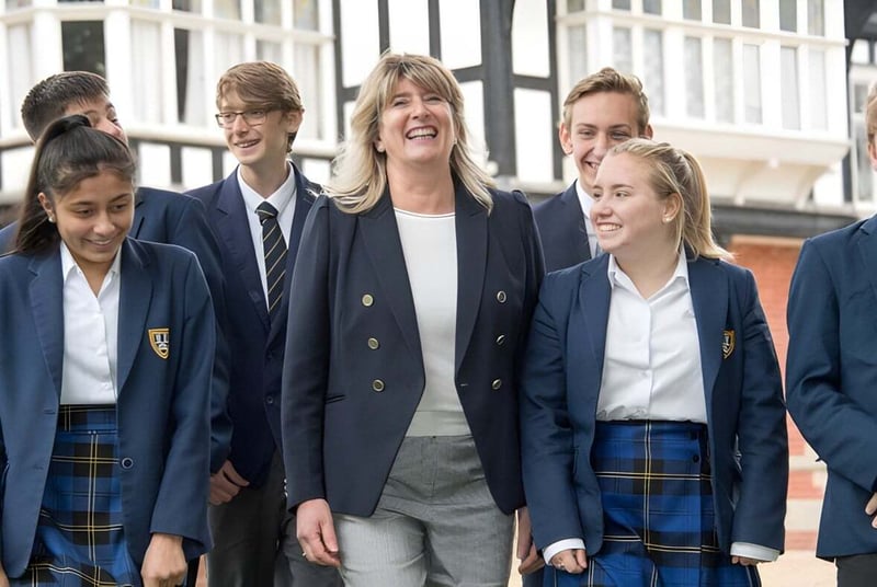 Un grupo de estudiantes se encuentra alegremente frente a un edificio con grandes ventanas en el campus de la Bedstone School.