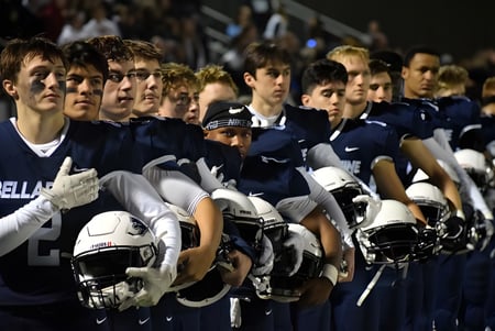 Un grupo de jóvenes atletas de la Bellarmine Preparatory School está de pie con cascos en un campo deportivo por la noche.