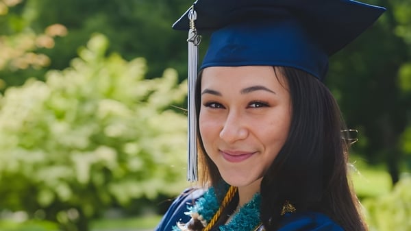 Una graduada de la Bellarmine Preparatory School con toga de graduación azul está en un área verde y sonríe.
