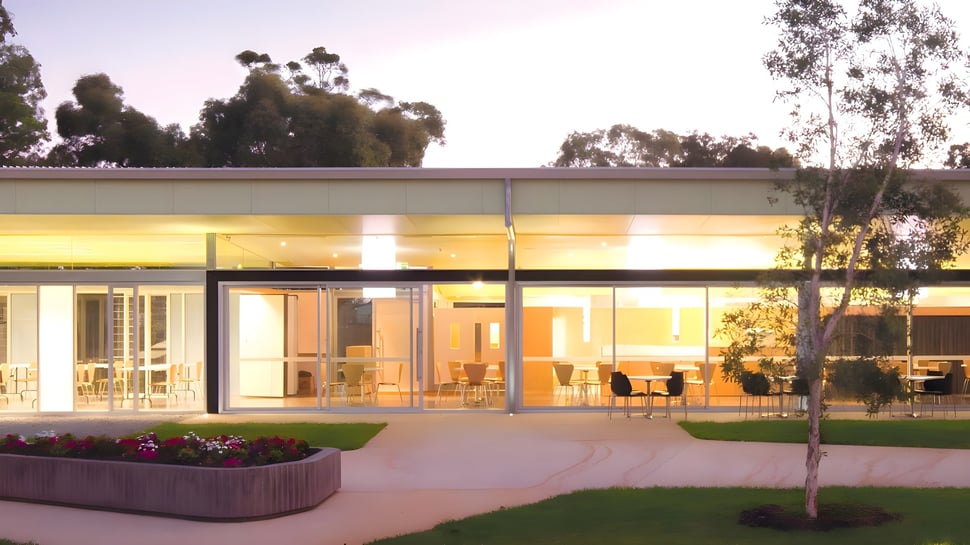 El moderno edificio de cristal del Belmont City College con área verde y plantas en primer plano.