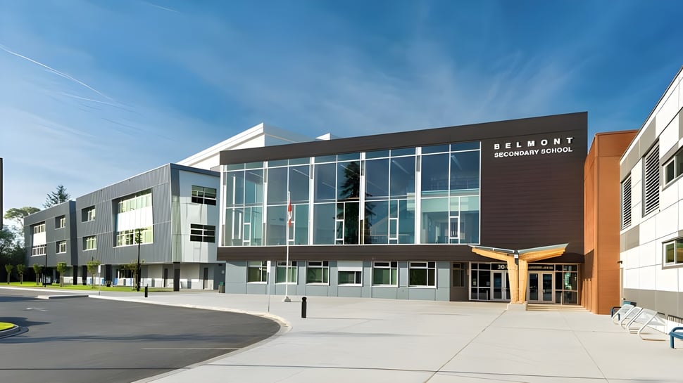 El moderno edificio de varios pisos con fachada de vidrio de la Belmont Secondary School está rodeado de un área pavimentada y vegetación.