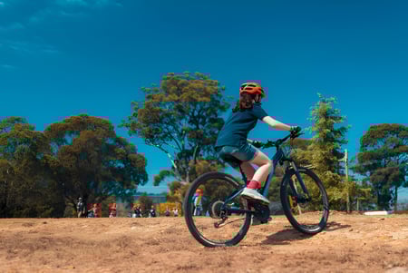 Una persona vestida con ropa deportiva monta en bicicleta por un camino rodeado de árboles en el terreno de la Benowa State High School.