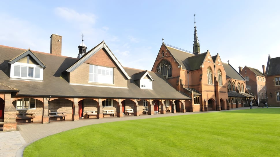 El patio de la Berkhamsted School muestra un patio cubierto de hierba rodeado de un edificio histórico de ladrillo con arcos.