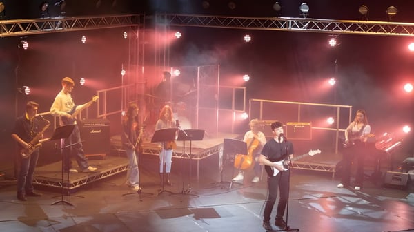 Músicos de la Berkhamsted School se presentan en un escenario iluminado con varios instrumentos y equipo.