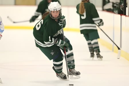 Dos jugadores de hockey de Berkshire School con camisetas verde y blancas juegan sobre el hielo de una pista de hielo.