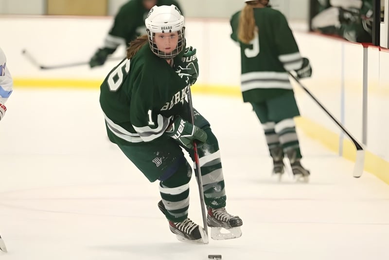 Dos jugadores de hockey de Berkshire School con camisetas verde y blancas juegan sobre el hielo de una pista de hielo.