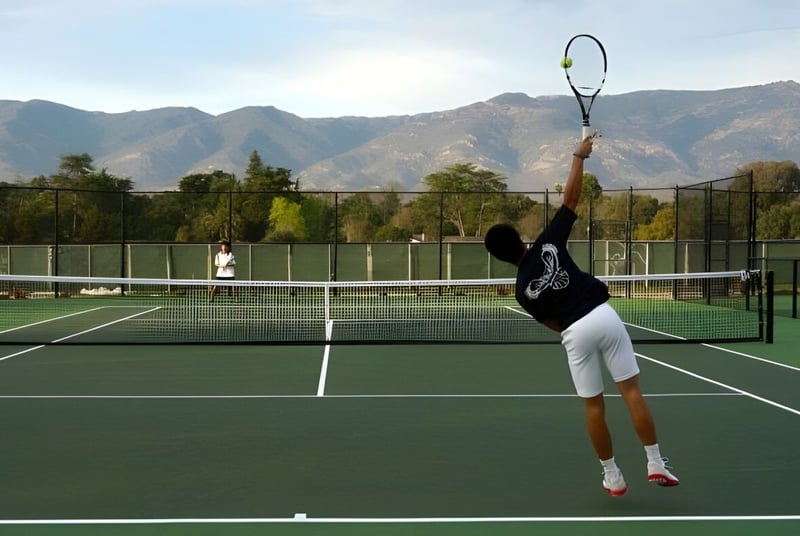 Una persona con ropa deportiva juega al tenis en el campo de tenis de la Besant Hill School con montañas y vegetación de fondo.