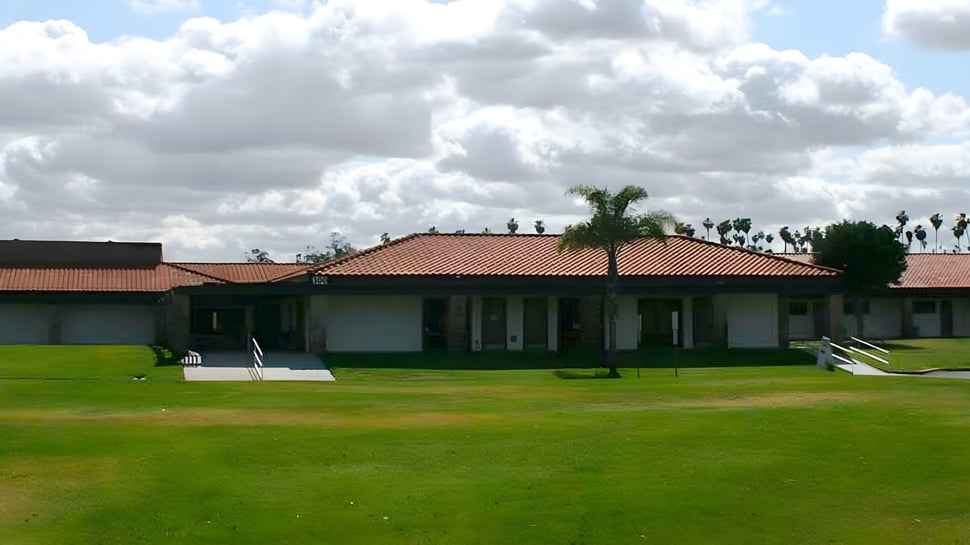 Un edificio de una planta con techo de tejas y palmeras en el terreno de las Bethel Christian Schools bajo un cielo nublado.