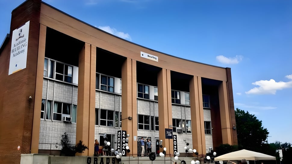 El edificio de ladrillo de varios pisos con grandes ventanas y fachada curva de la Beurling Academy se encuentra frente a un cielo despejado.
