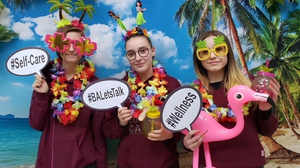 Tres estudiantes de la Beurling Academy llevan coloridos trajes hawaianos frente a un fondo de playa tropical.