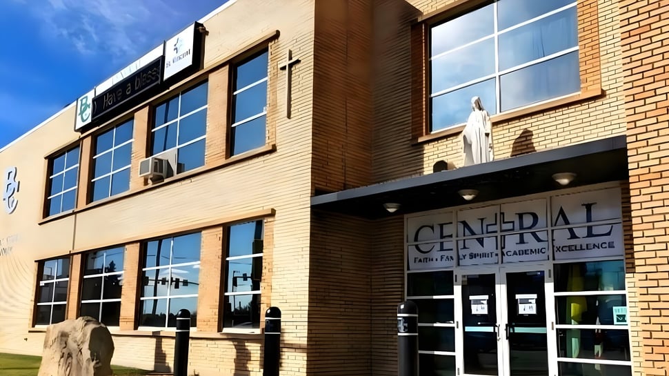 El edificio de ladrillo de varios pisos de la Billings Central Catholic High School con grandes ventanas y un letrero bien visible se ve frente al cielo azul.