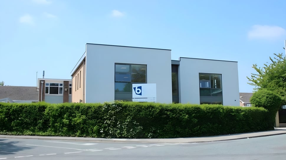 El moderno edificio del Birkenhead College con grandes ventanas y un cuidado seto bajo un cielo azul.