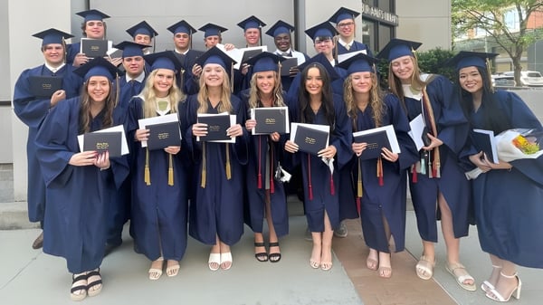 Un grupo de graduados de la Bishop Heelan Catholic High School está al aire libre en vestimenta académica y sostiene sus diplomas.