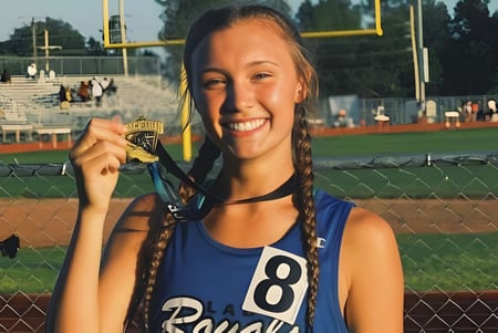 Una alumna de la Bishop J Snyder High School está con una medalla frente a un campo de béisbol.
