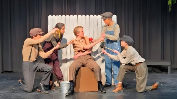 Estudiantes de la Bishop Kelly High School presentan una obra de teatro en un escenario con una cerca de madera como telón de fondo.