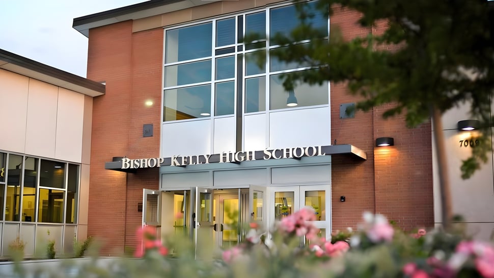La vista exterior del edificio escolar de Bishop Kelly High School con flores rosas floreciendo en primer plano.