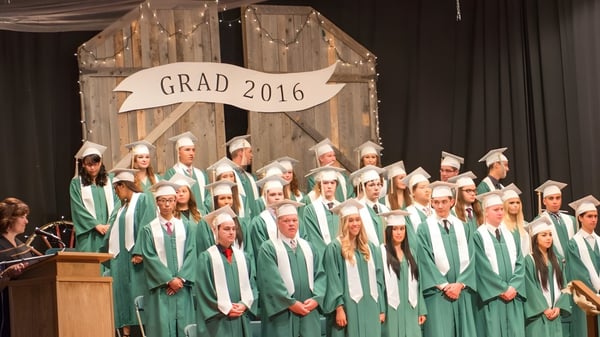Graduados de la Bishop Mahoney High School están en togas verdes en el escenario frente a un banner que dice Grad 2016.