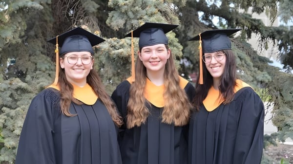Tres egresadas de la Bishop O'Byrne High School están juntas al aire libre en un entorno boscoso.