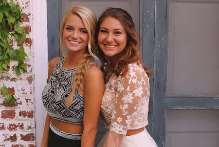 Dos estudiantes de la Bishop Rosecrans High School están frente a una puerta de madera desgastada rodeada de vegetación exuberante.