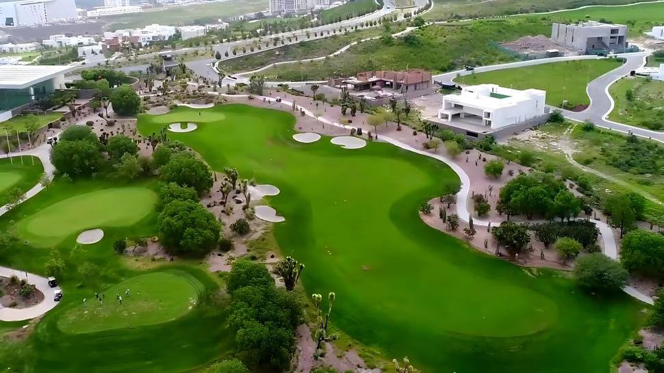 El campo de golf de la Bishop’s Gate Golf Academy se ve con greens y fairways bien cuidados ante un paisaje urbano.