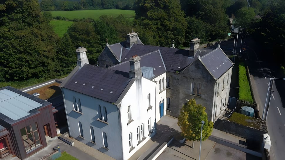 Un edificio residencial de varios pisos con techo de pizarra y chimeneas en un paisaje boscoso en el terreno de la Blackwater Community School.