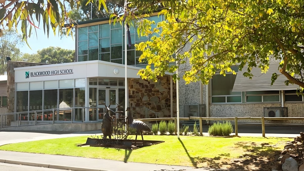 El moderno edificio de fachada de vidrio de la Blackwood High School con césped y árboles en primer plano frente a un paisaje verde.