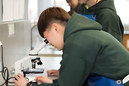 Un estudiante de la Blackwood High School examina concentrado muestras con un microscopio en el laboratorio escolar.