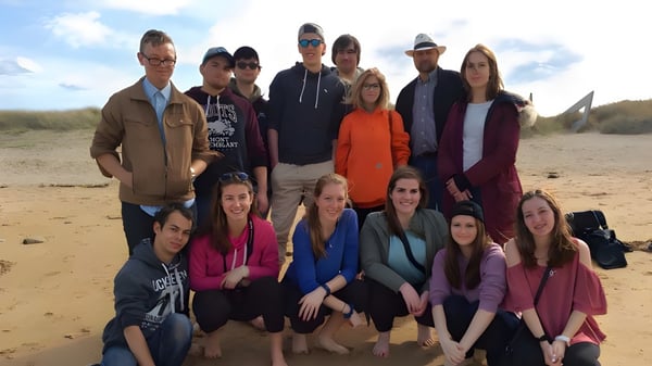 Un grupo de estudiantes de la Blenheim District High School está junto a una playa arenosa bajo un cielo nublado.