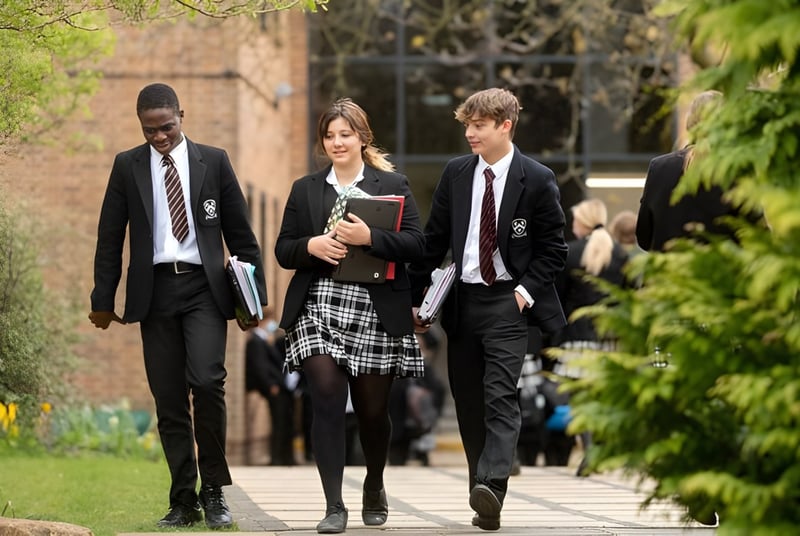 Tres personas pasean juntas por un camino con mucho verde en el terreno de la Bloxham School.