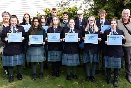 Un grupo de estudiantes de Blue Mountain College está junto con certificados frente a un edificio al aire libre.
