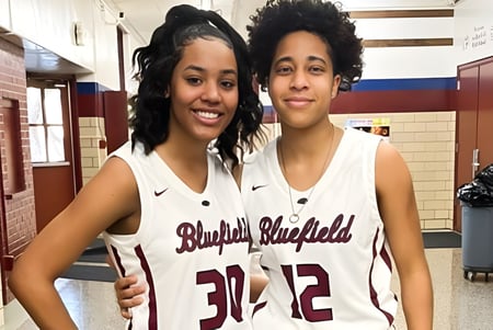 Dos alumnas en camisetas de baloncesto de Bluefield High School están juntas en el pasillo de la escuela.