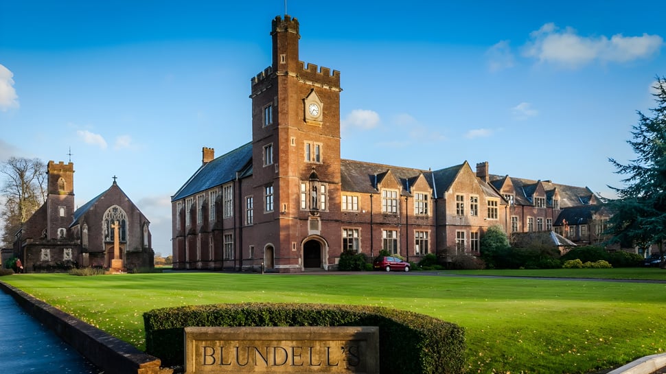 El histórico edificio de ladrillo con un alto reloj en el campus de la Blundells School está rodeado de césped bien cuidado y abundante vegetación.