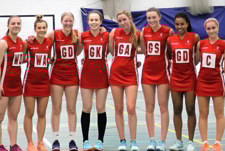 Un grupo de jóvenes atletas femeninas posan en camisetas rojas en el gimnasio de la Blundells School.