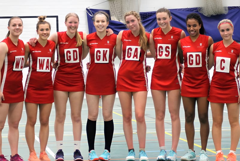 Un grupo de jóvenes atletas femeninas posan en camisetas rojas en el gimnasio de la Blundells School.