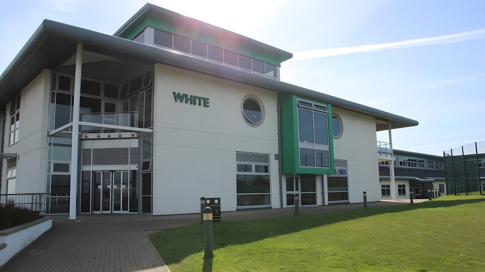 El moderno edificio de varios pisos de Bodmin College con fachada verde y blanca se encuentra en un césped bien cuidado con caminos pavimentados.