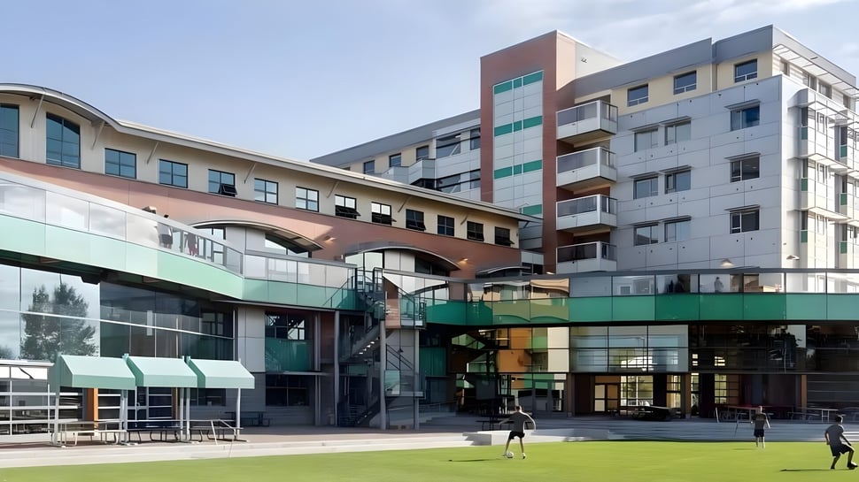 El moderno edificio escolar de varios pisos de la Bodwell High School con arcos y balcones rodeado de un área verde con personas.