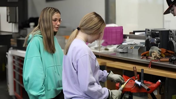 Dos estudiantes del Boise School District están en una sala de trabajo con varios objetos y dispositivos de fondo.